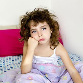 little girl frowning sitting up in bed with leaning on her hand on her cheek because she has lice